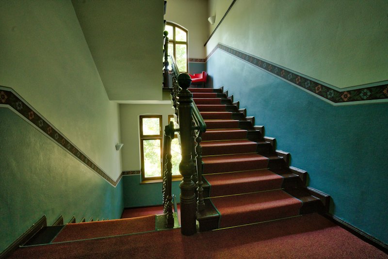 Escalera de un edificio antiguo sin ascensor, con barandilla de madera y peldaños enmoquetados